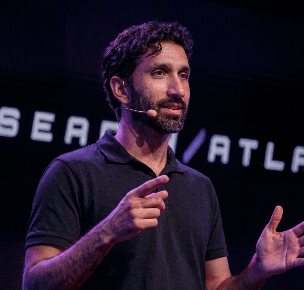 Manick Bhan delivering a talk at a conference on stage.