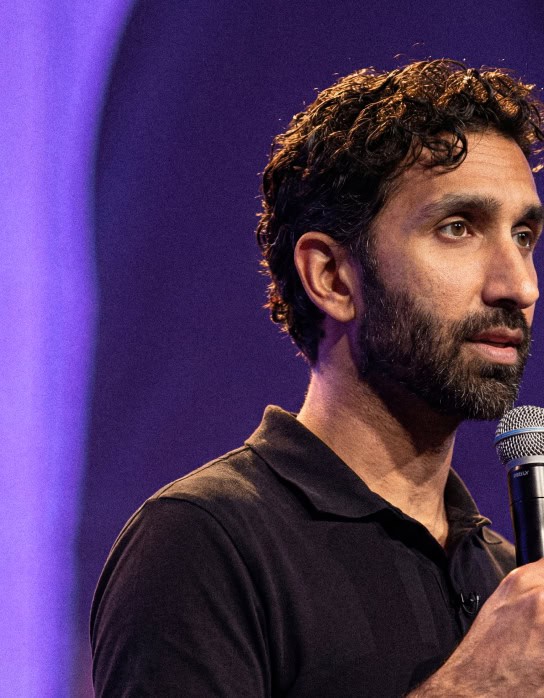Manick Bhan delivering a speech at a conference, holding a microphone.